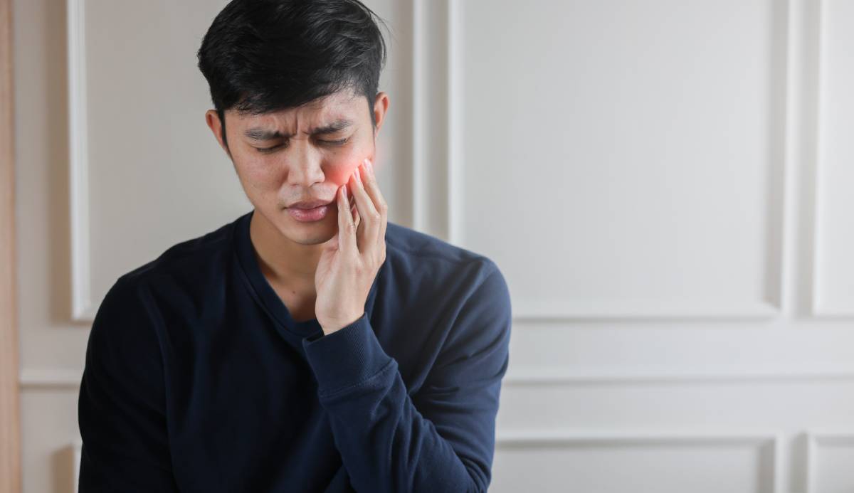 close up young man frowning in pain and using hand to massage on cheek.